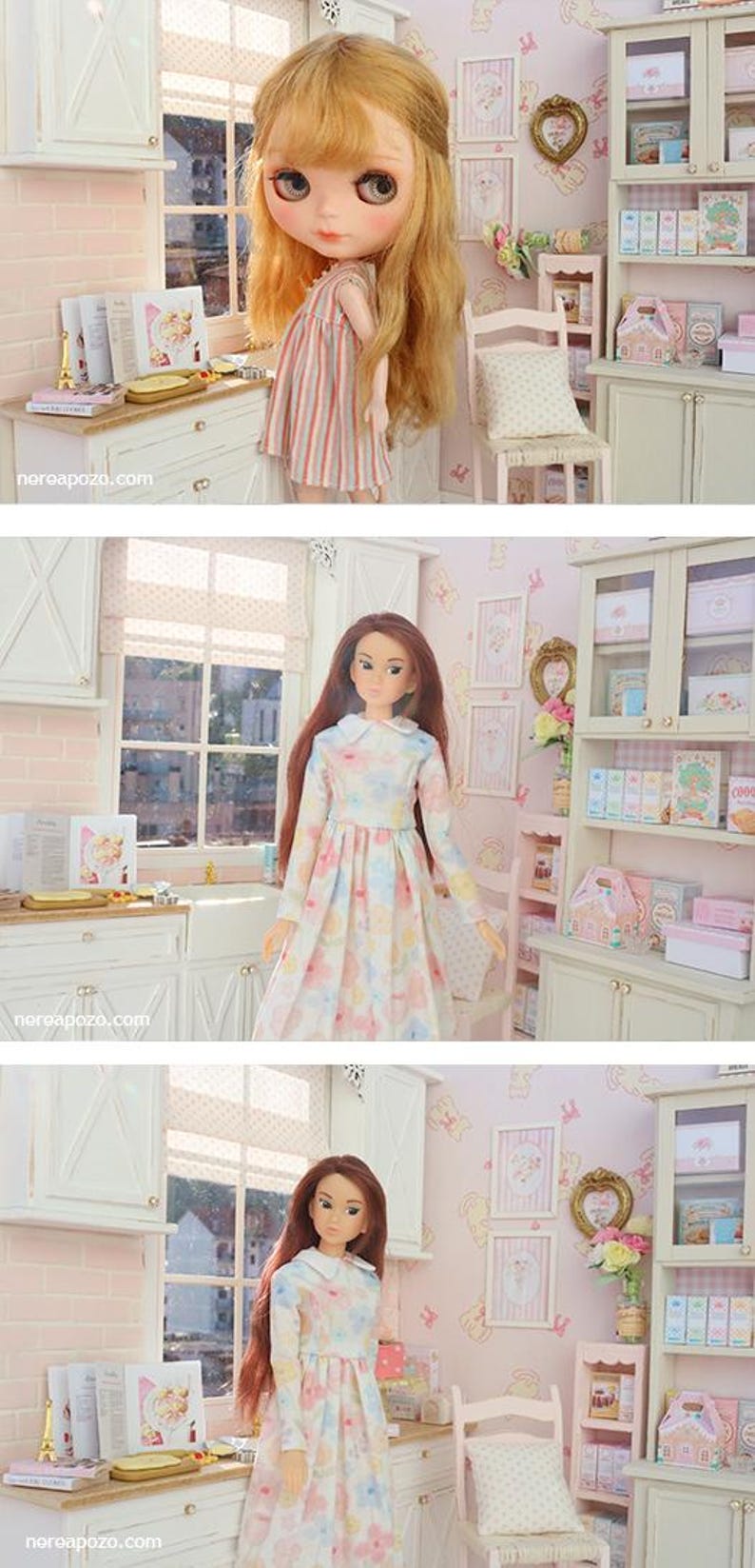 May include: A dollhouse kitchen scene with two dolls. One doll is in a striped dress, the other in a floral dress. The kitchen has white cabinets, a window, and decorative items, including books and a miniature chair.