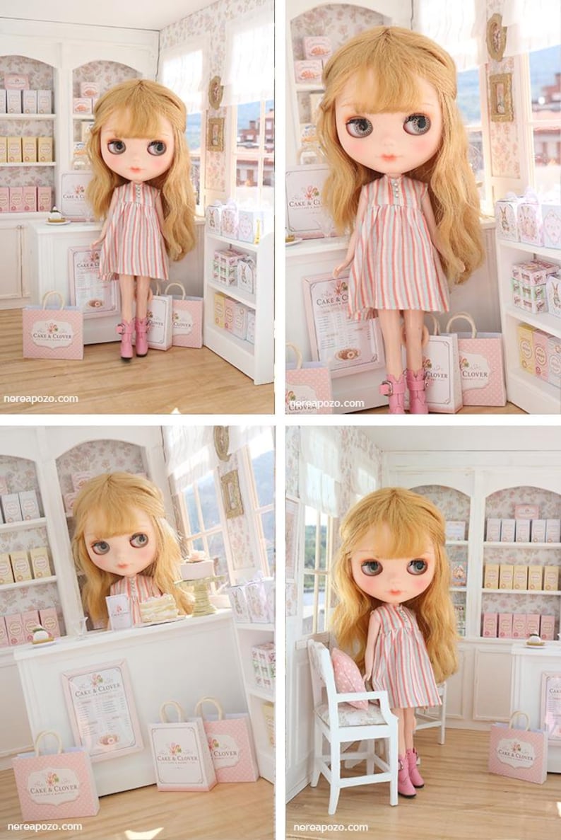 K&ouml;nnte beinhalten: Eine Puppe mit langem, welligem blonden Haar und gro&szlig;en Augen tr&auml;gt ein &auml;rmelloses Kleid mit vertikalen rosa, wei&szlig;en und blauen Streifen sowie rosa Stiefel. Die Puppe befindet sich in einer Miniatur-B&auml;ckerei mit Regalen und kleinen Einkaufst&uuml;ten.