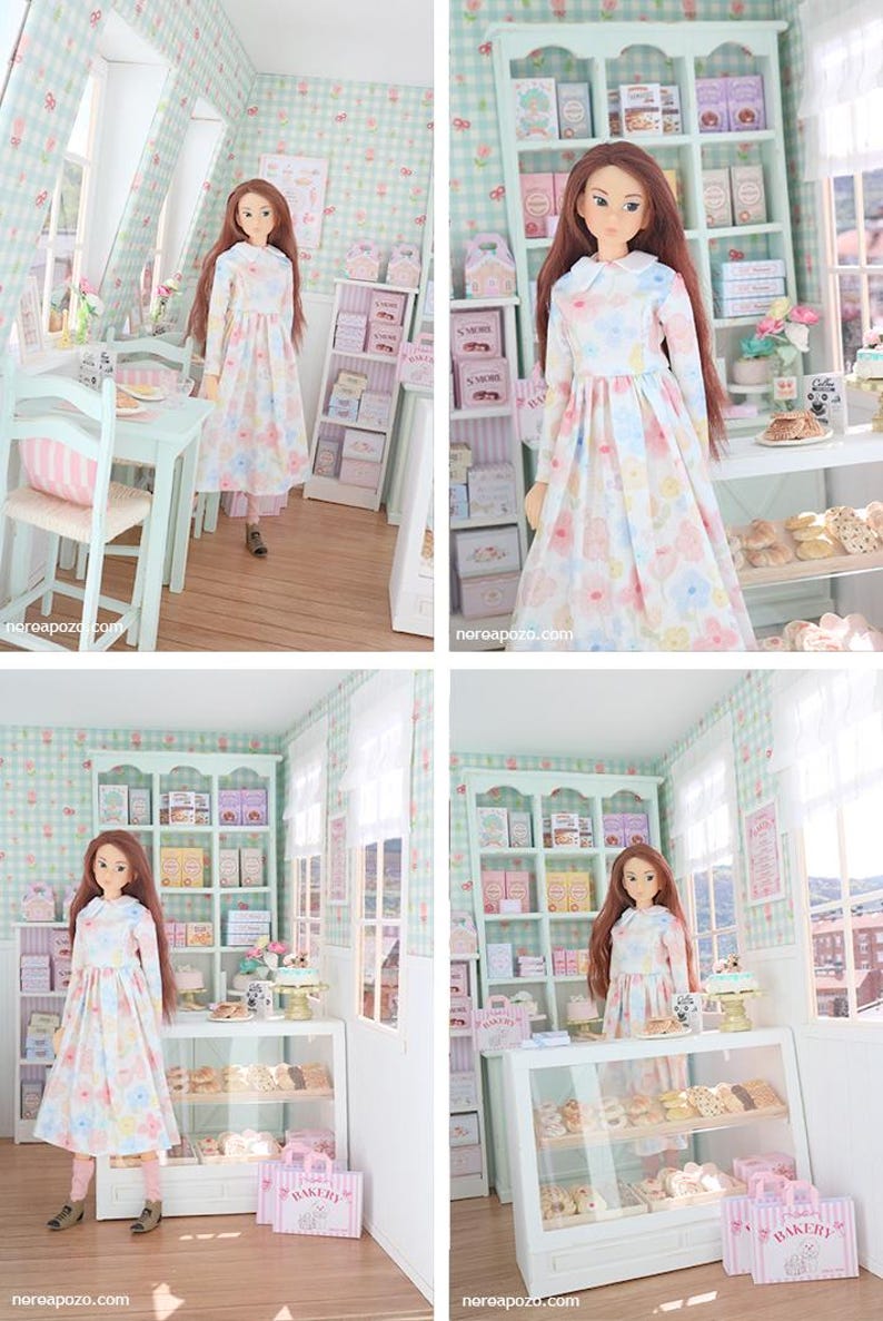 K&ouml;nnte beinhalten: Eine Puppe in einem Blumenkleid steht in einer Miniatur-B&auml;ckerei. Die B&auml;ckerei verf&uuml;gt &uuml;ber Regale mit verpackten Waren, eine Vitrine mit Geb&auml;ck und rosa B&auml;ckereitaschen. Die W&auml;nde sind mit einem hellgr&uuml;nen und wei&szlig;en Karomuster verziert.