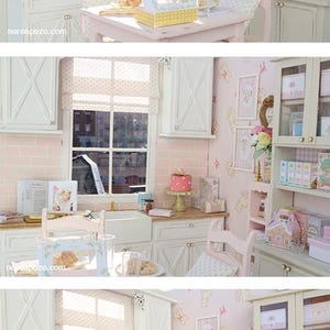 May include: A miniature kitchen scene in pink and white. The scene features a table, chairs, cabinets, and a window. A cake, boxes, and other items are on display. The walls are pink with a repeating pattern.