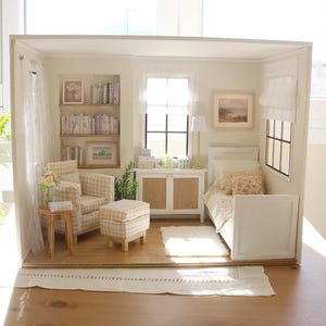 K&ouml;nnte beinhalten: Ein Miniatur-Puppenhauszimmer mit einem beigefarbenen karierten Sessel und Hocker, einem Einzelbett mit Blumenbettw&auml;sche, einem h&ouml;lzernen Beistelltisch, einem wei&szlig;en Schrank und eingebauten B&uuml;cherregalen, die mit winzigen B&uuml;chern gef&uuml;llt sind.