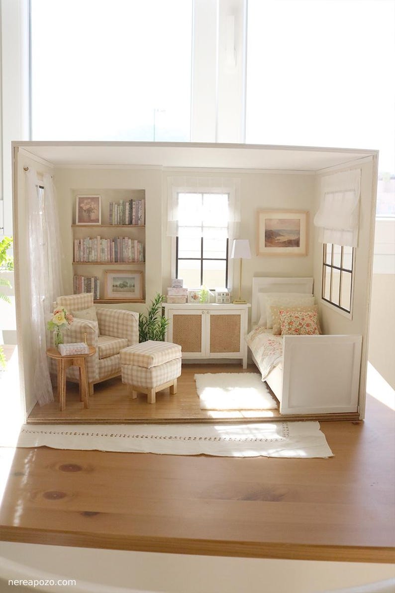 K&ouml;nnte beinhalten: Ein Miniatur-Puppenhauszimmer mit einem beigefarbenen karierten Sessel und Hocker, einem Einzelbett mit Blumenbettw&auml;sche, einem h&ouml;lzernen Beistelltisch, einem wei&szlig;en Schrank und eingebauten B&uuml;cherregalen, die mit winzigen B&uuml;chern gef&uuml;llt sind.