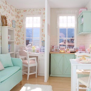 May include: A detailed dollhouse interior with a living room and kitchen. The living room has a teal sofa with cushions, a white bookshelf, and floral wallpaper. The kitchen features a mint green cabinet and a white table.