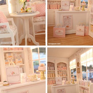 K&ouml;nnte beinhalten: Eine Miniatur-B&auml;ckerei mit wei&szlig;er Theke, Regalen voller Schachteln, einem Tisch mit St&uuml;hlen und Einkaufst&uuml;ten mit der Aufschrift Cake & Clover. Die Einrichtung umfasst florale Tapeten, eine Men&uuml;tafel und kleine Kuchen in einer Puppenstube.