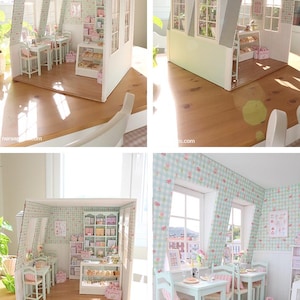 K&ouml;nnte beinhalten: Ein Miniatur-Puppenhaus-B&auml;ckerei in hellblau und wei&szlig;. Im Inneren befinden sich Tische, St&uuml;hle und eine Vitrine mit Miniaturgeb&auml;ck. Die W&auml;nde sind mit einem Blumenmuster verziert, und die Fenster bieten einen Blick nach drau&szlig;en.