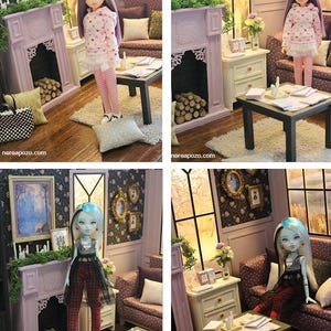 May include: A dollhouse living room scene featuring a lavender fireplace with logs, a dark coffee table with papers, a sofa with pillows, and wall art. Two different dolls are shown in the room, one with purple hair and one with blue-streaked hair.