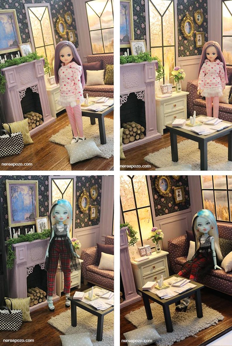 May include: A dollhouse living room scene featuring a lavender fireplace with logs, a dark coffee table with papers, a sofa with pillows, and wall art. Two different dolls are shown in the room, one with purple hair and one with blue-streaked hair.