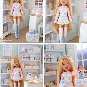 May include: A blonde doll with long hair wearing a light pink long-sleeve shirt with a graphic print, a ruffled skirt, striped leg warmers, and light blue boots. The doll is positioned in a miniature bakery setting with shelves of baked goods.