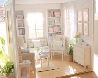 Könnte beinhalten: Miniatur-Puppenhaus-Wohnzimmer mit hellem Holzboden, einem beigen Sofa und einem weißen Sessel mit floralen Kissen. Der Raum verfügt über einen kleinen weißen Tisch, Bücherregale und eine weiße Kommode. Die Wände sind hellgrün gestrichen und mit floraler Tapete dekoriert.