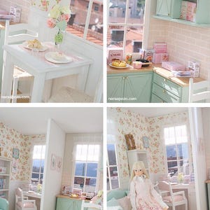 May include: A miniature dollhouse kitchen and dining room scene. The rooms feature white furniture, floral wallpaper, and pastel green cabinets. A doll is seated on a teal sofa. The scene includes a table setting, a window, and decorative items.
