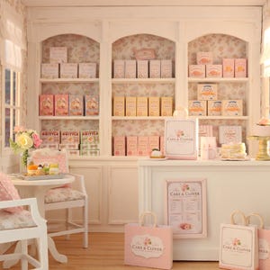 K&ouml;nnte beinhalten: Eine Miniatur-B&auml;ckerei-Auslage mit wei&szlig;en Regalen voller verpackter Waren, einer Verkaufstheke mit Cake & Clover-Branding, Einkaufstaschen, einem kleinen Tisch mit zwei St&uuml;hlen und einer gebl&uuml;mten Tapete in einer sanften Pastellfarbpalette.