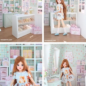 K&ouml;nnte beinhalten: Eine Miniatur-B&auml;ckerei-Szene mit einer Puppe in einem Kleid mit Katzenmuster. Die B&auml;ckerei verf&uuml;gt &uuml;ber Vitrinen mit Geb&auml;ck, Regale mit Kisten und rosa "Bakery"-Taschen. Die W&auml;nde sind mit einem hellgr&uuml;nen und wei&szlig;en Karomuster verziert.