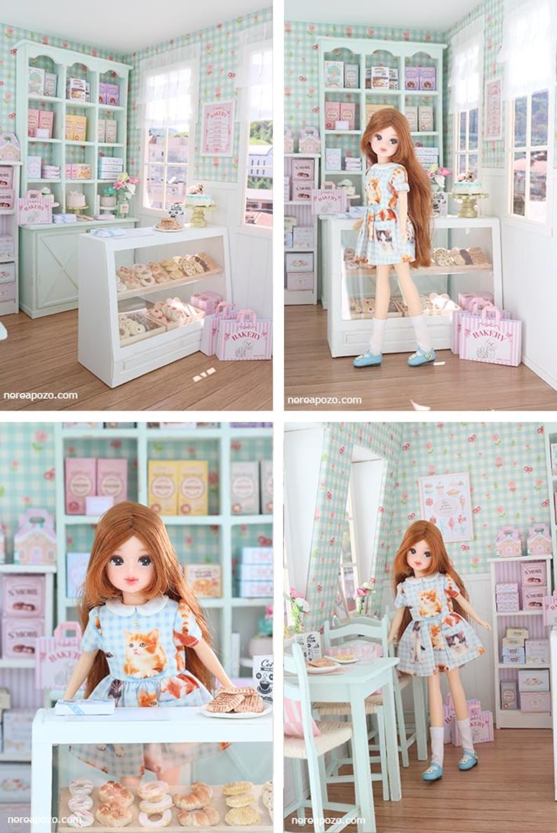 K&ouml;nnte beinhalten: Eine Miniatur-B&auml;ckerei-Szene mit einer Puppe in einem Kleid mit Katzenmuster. Die B&auml;ckerei verf&uuml;gt &uuml;ber Vitrinen mit Geb&auml;ck, Regale mit Kisten und rosa "Bakery"-Taschen. Die W&auml;nde sind mit einem hellgr&uuml;nen und wei&szlig;en Karomuster verziert.