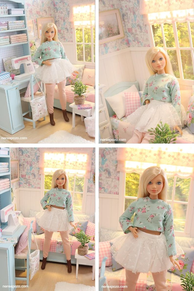 K&ouml;nnte beinhalten: Eine Puppe mit blonden Haaren, die ein hellblaues, gebl&uuml;mtes Crop-Top, einen wei&szlig;en T&uuml;llrock und rosa Leggings tr&auml;gt. Die Puppe befindet sich in einem Miniaturzimmer mit N&auml;hmaschine, Bett und Fenster. Der Raum ist in Pastellfarben gehalten.