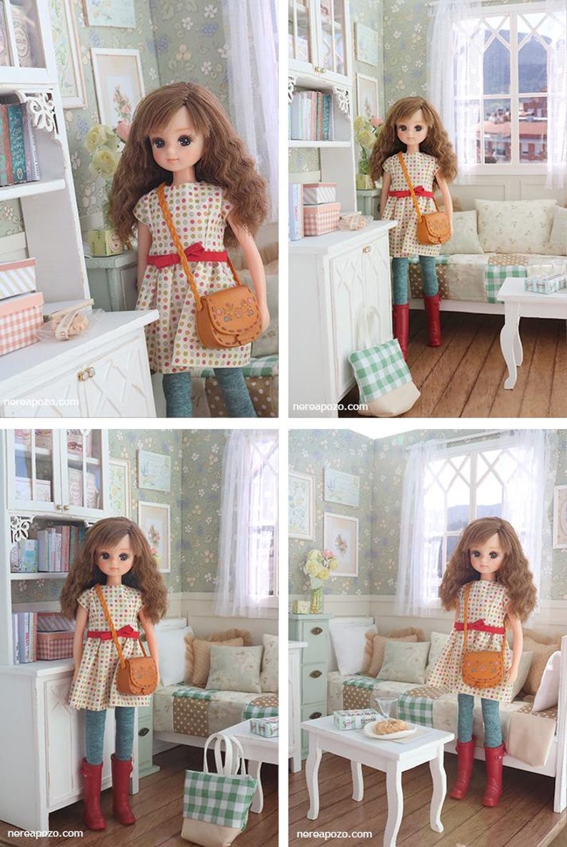 Może przedstawiać: Lalka z brązowymi kręconymi włosami, ubrana w sukienkę w kropki, czerwony pasek i brązową torebkę. Lalka znajduje się w miniaturowym pokoju z białą szafką, p&oacute;łkami na książki i małym białym stolikiem.