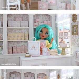 K&ouml;nnte beinhalten: Eine Miniatur-B&auml;ckerei-Szene mit einer Puppe mit t&uuml;rkisfarbenem Haar, die eine gelbe Strickjacke und einen rosa Rock tr&auml;gt und eine kleine rosa Katzenfigur h&auml;lt. Der Laden umfasst wei&szlig;e Regale mit Schachteln, eine Theke und kleine Torten.