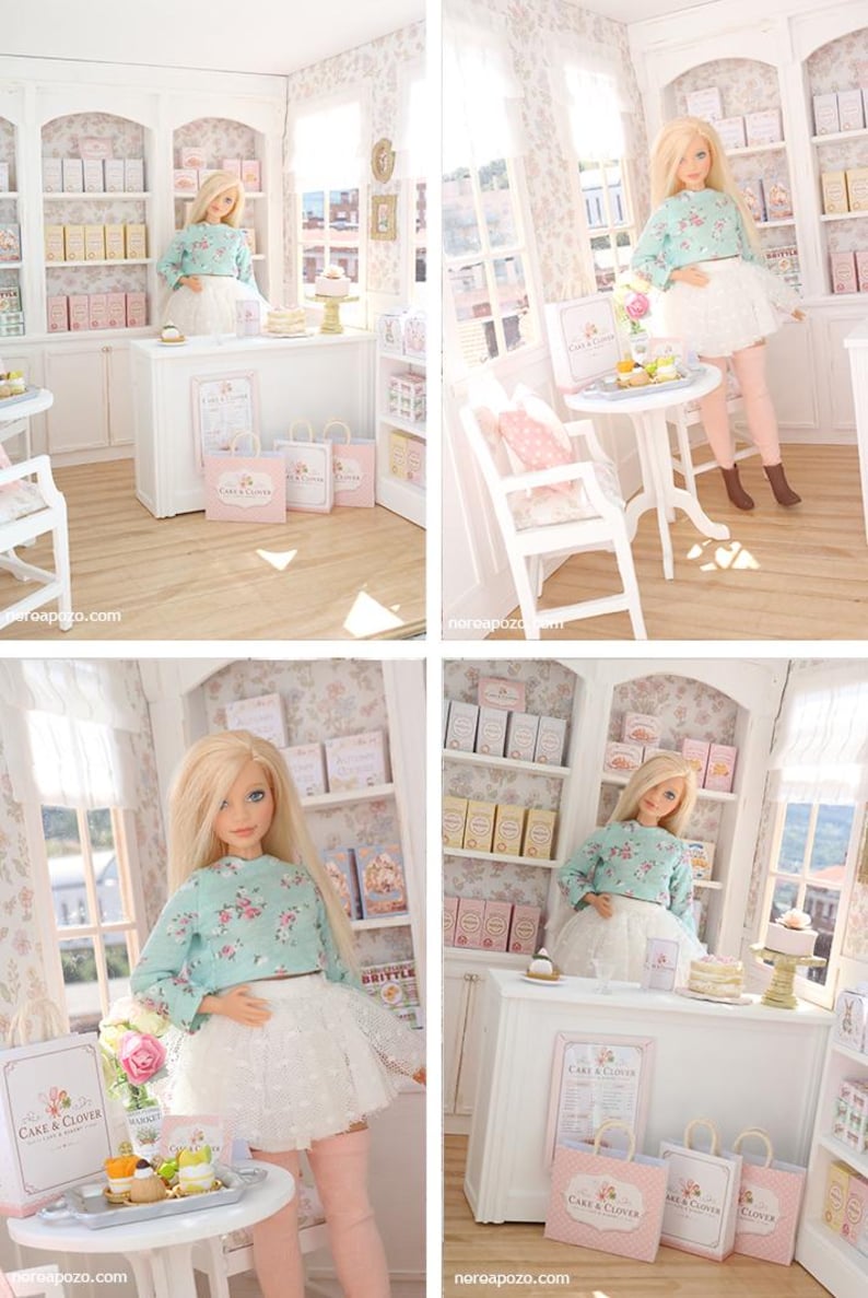K&ouml;nnte beinhalten: Eine Miniatur-Puppenhaus-B&auml;ckerei mit einer blonden Puppe in einem lang&auml;rmeligen Blumenoberteil und einem wei&szlig;en Spitzenrock. Der Laden enth&auml;lt wei&szlig;e Regale, eine Verkaufstheke, kleine Tische, St&uuml;hle und Einkaufst&uuml;ten mit der Aufschrift Cake & Clover.