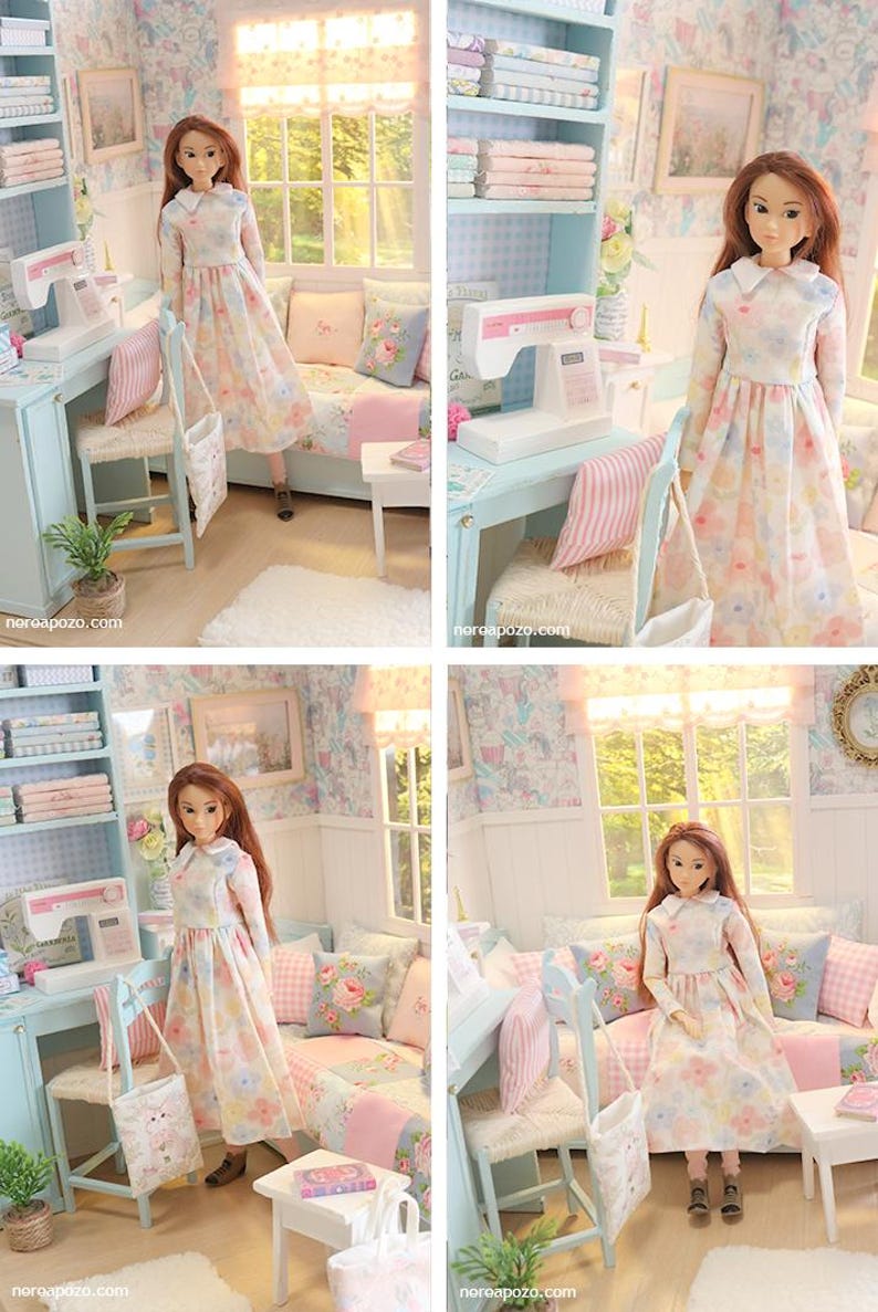 K&ouml;nnte beinhalten: Eine Puppe in einem Blumenkleid steht in einem Miniaturzimmer mit einer N&auml;hmaschine, einem Stuhl und einem Sofa. Der Raum ist in Pastellfarben mit Blumentapeten und gerahmten Bildern dekoriert.