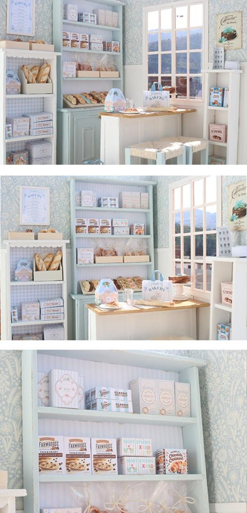 May include: A miniature bakery diorama featuring light blue wooden shelving units filled with small boxes of cookies, bread loaves, and pastries. The scene includes a small wooden table with stools, a window, and various printed signs labeled Bakery, S'more, and Farmhouse.