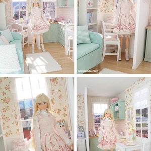 May include: A doll in a pink dress with a heart and music note design stands in a miniature room. The room features a kitchen, living room, and floral wallpaper. The doll has long blonde hair and white boots. The room is decorated in pastel colours.
