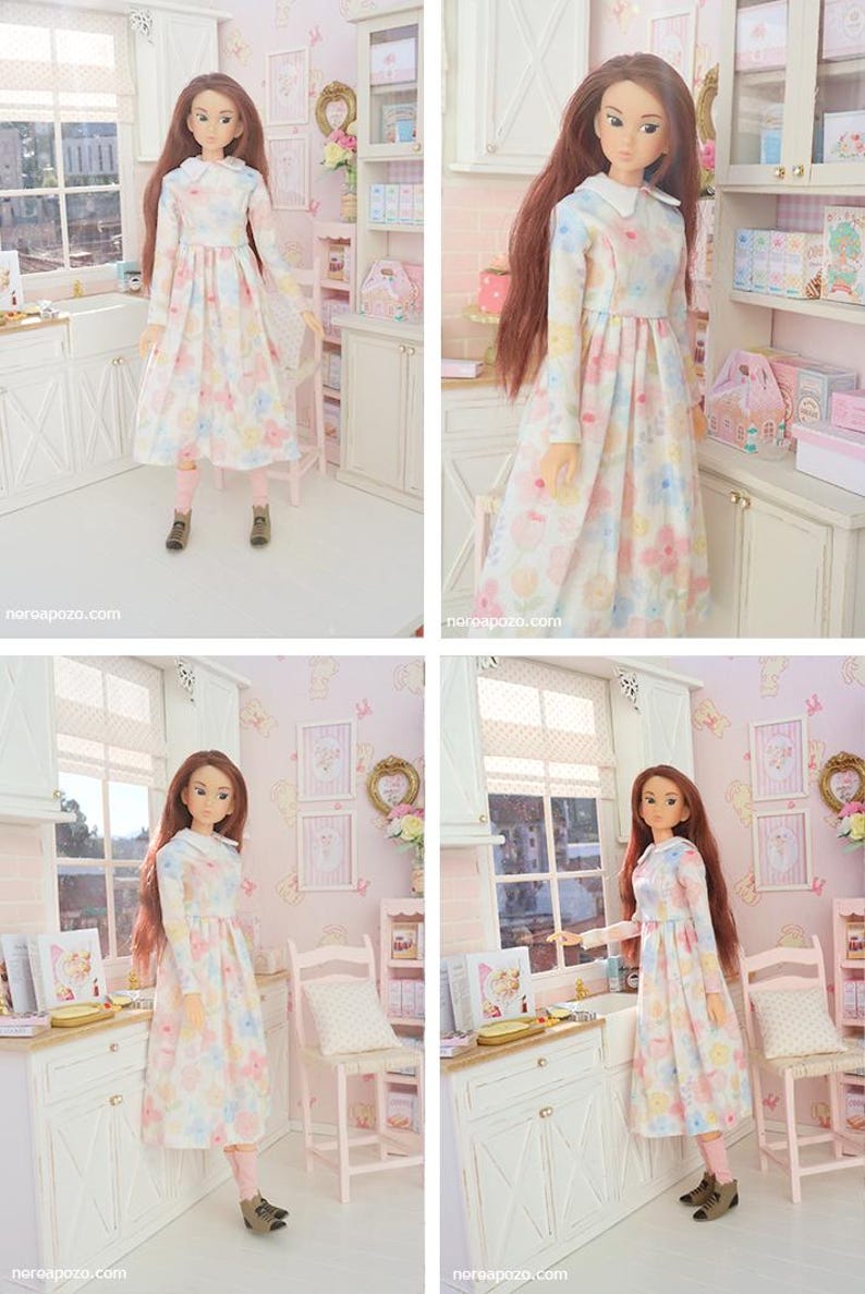 May include: A doll in a miniature kitchen, wearing a long-sleeved dress with a floral pattern. The dress has a white collar and pastel floral design. The doll has long brown hair, pink leggings, and brown boots. The setting is a miniature kitchen.