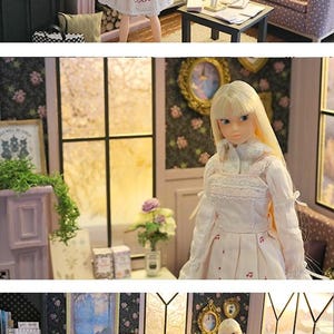 May include: A blonde doll with long hair wearing a white long-sleeved dress with a pink floral pattern on the skirt, a high collar, and lace trim. The doll stands in a miniature room setting featuring a fireplace, a sofa, and a bookshelf.