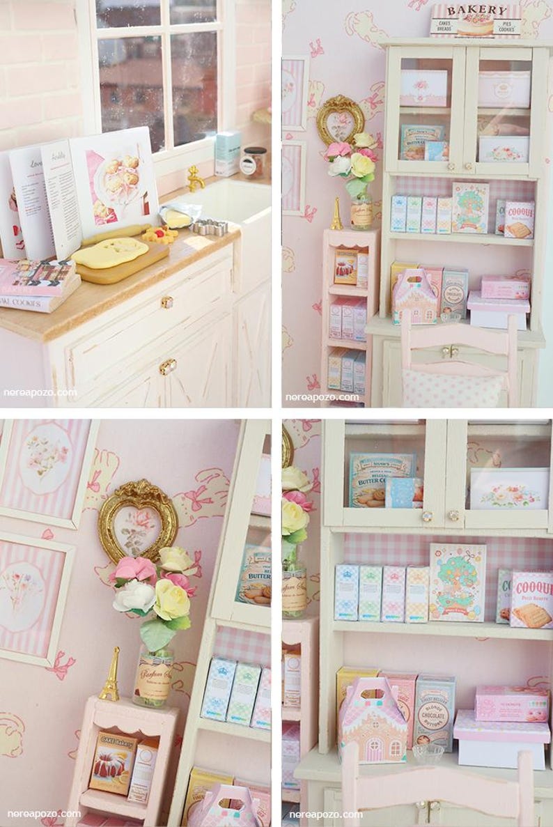 May include: A miniature bakery scene with a white cabinet, shelves, and a small pink chair. The shelves are filled with boxes, books, and decorative items. The walls are pink with framed pictures and a floral arrangement. A small kitchen area is also visible.
