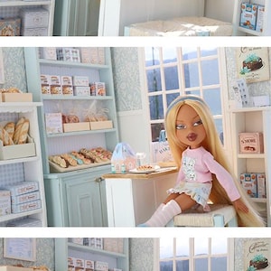 May include: A miniature bakery playset featuring shelves stocked with small boxes of cookies, bread loaves, and pastries. The scene includes a counter, a window, and a doll with long blonde hair wearing a pink long-sleeve shirt and a patterned skirt.