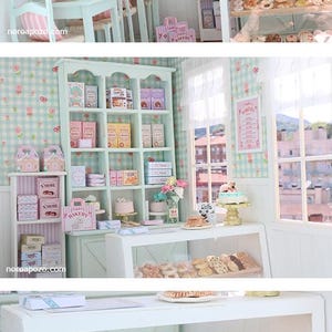 K&ouml;nnte beinhalten: Miniatur-B&auml;ckerei-Szene mit pastellgr&uuml;ner und rosa Dekoration. Vitrinen pr&auml;sentieren verschiedene Backwaren, darunter Kekse, Geb&auml;ck und Kuchen. Regale sind mit Schachteln und T&uuml;ten best&uuml;ckt. Tische und St&uuml;hle sind f&uuml;r Kunden gedeckt.