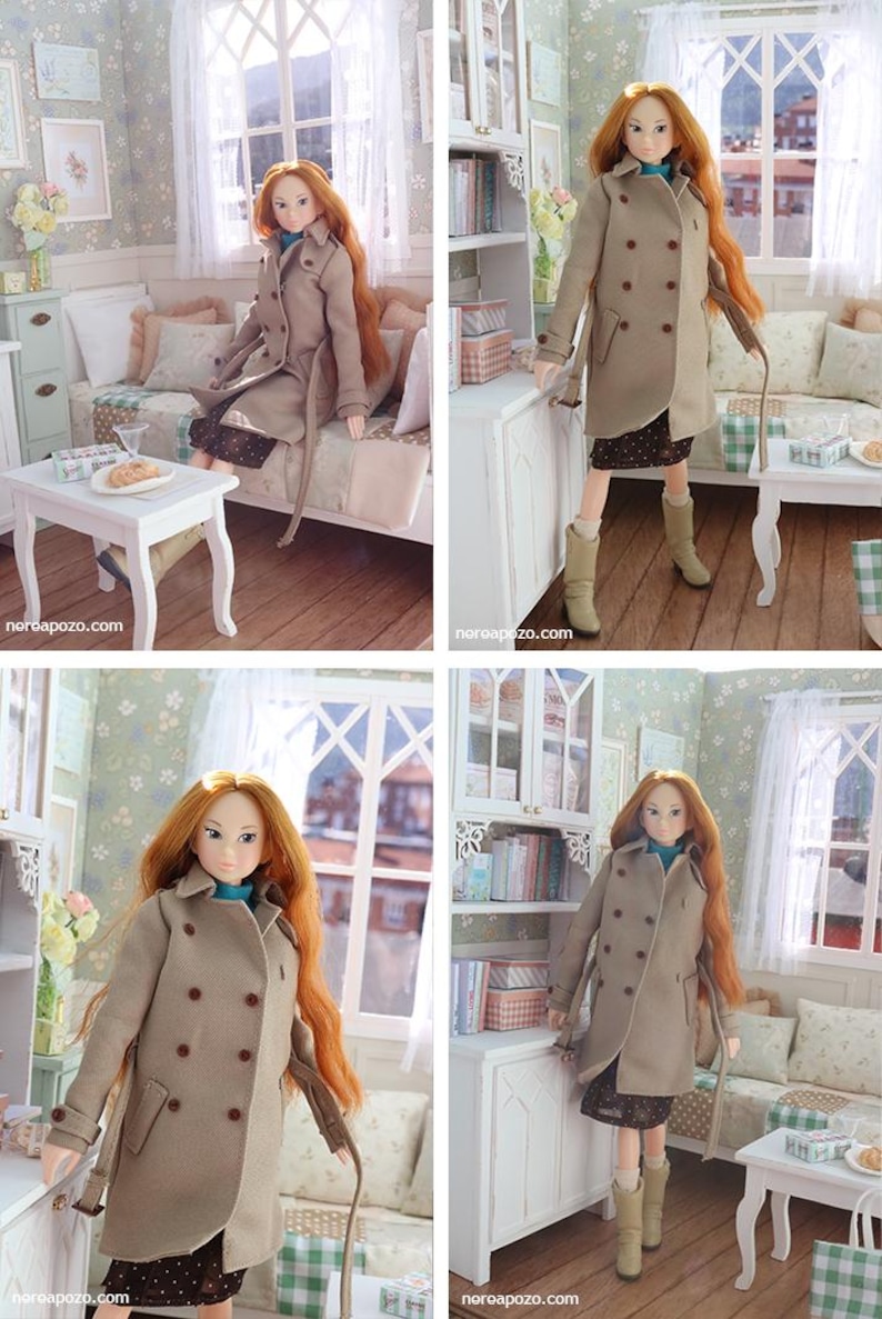 Może przedstawiać: Lalka z długimi rudymi włosami w beżowym trenczu, ciemnej sp&oacute;dnicy i beżowych butach. Lalka znajduje się w miniaturowym pokoju z białym stołem, sofą i oknem.