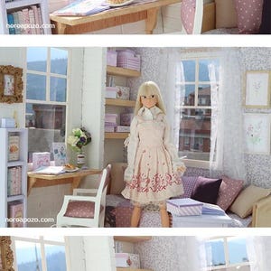 Pode incluir: Cena de casa de bonecas em miniatura com uma boneca vestida com um vestido rosa. O quarto apresenta uma mesa com uma bolacha, livros e um vaso de flores. Prateleiras com caixas e livros. Uma janela oferece uma vista de uma montanha.