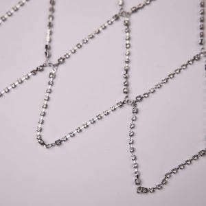 May include: Silver body jewelry featuring multiple strands of small, sparkling rhinestones. The delicate chains are connected at various points, creating a layered effect. The jewelry is designed to be worn on the body.