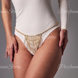 Könnte beinhalten: Ein goldener Ketten-Körper-Schmuck mit einem Fransenbesatz aus Strasssteinen. Die Kette wird um die Hüften getragen und die Fransen hängen bis zu den Oberschenkeln.