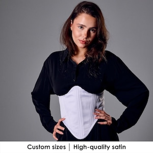 May include: A white satin corset with vertical seams is worn over a black top. The corset has a pointed bottom and a structured design. The text at the bottom reads "Custom sizes | High-quality satin".