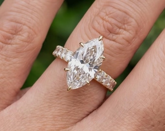 May include: A gold ring featuring a large marquise-cut center diamond held by four prongs, with a band encrusted with smaller round-cut diamonds along the visible top half. The metal setting is a warm yellow gold tone, showcasing a classic design.