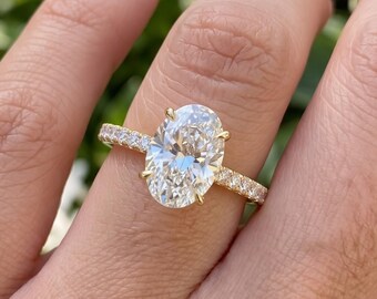May include: A gold ring featuring a large oval-cut center stone held by four prongs, with a band encrusted with smaller round-cut stones along the top half. The metal band has a polished yellow gold finish, and the stones are clear and faceted.