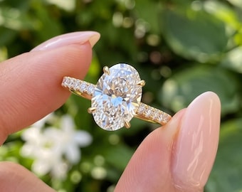 May include: A gold ring featuring a large oval-cut center stone held by four prongs, with a band accented by smaller round-cut stones along the sides. The metal band has a polished finish and the setting is designed to elevate the center stone.