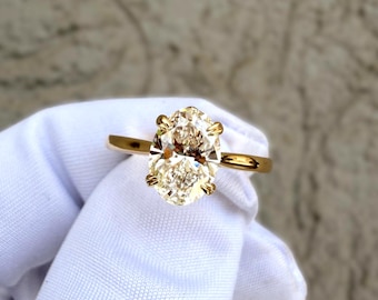 May include: A gold ring featuring a large, oval-cut, clear faceted gemstone held in place by four prongs. The band is a simple, polished gold metal. The stone is positioned centrally, showcasing its brilliant cut and reflective surface.