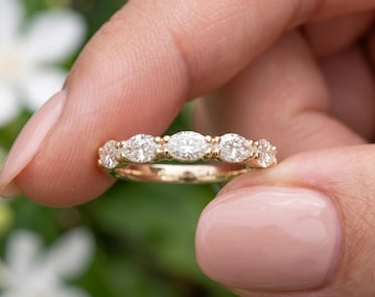 May include: A gold band ring featuring five marquise-cut clear stones arranged horizontally across the top. The stones are set in a shared prong setting, creating a continuous line of sparkle. The metal band has a polished yellow gold finish.