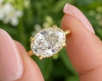 May include: A gold ring featuring a large, oval-cut, clear faceted gemstone held in place by four prongs. The band is thin and polished, showcasing a classic solitaire design that highlights the brilliance and clarity of the central stone.