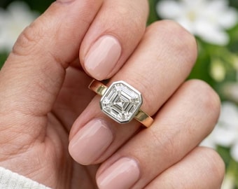 May include: A ring featuring a square-cut clear gemstone set in a silver-toned bezel, mounted on a polished gold band. The stone displays a distinct step-cut facet pattern, creating a geometric appearance within the metallic setting.