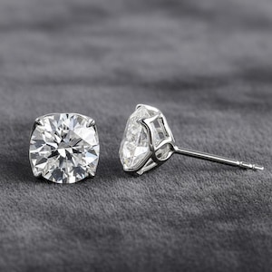 May include: A pair of diamond stud earrings. Each earring features a large, round-cut, clear diamond set in a silver or white gold prong setting. The earrings are displayed on a gray background.