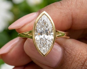 May include: A marquise-cut clear gemstone set in a yellow gold bezel setting. The ring features a smooth, polished gold band that tapers slightly as it meets the central stone, creating a clean and continuous look for the jewelry piece.