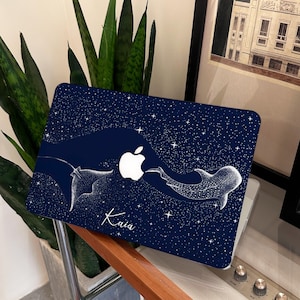 May include: A navy blue laptop case with a white Apple logo and a starry sky pattern. The case features a white illustration of a manta ray and a whale shark. The name "Kaia" is written in cursive.