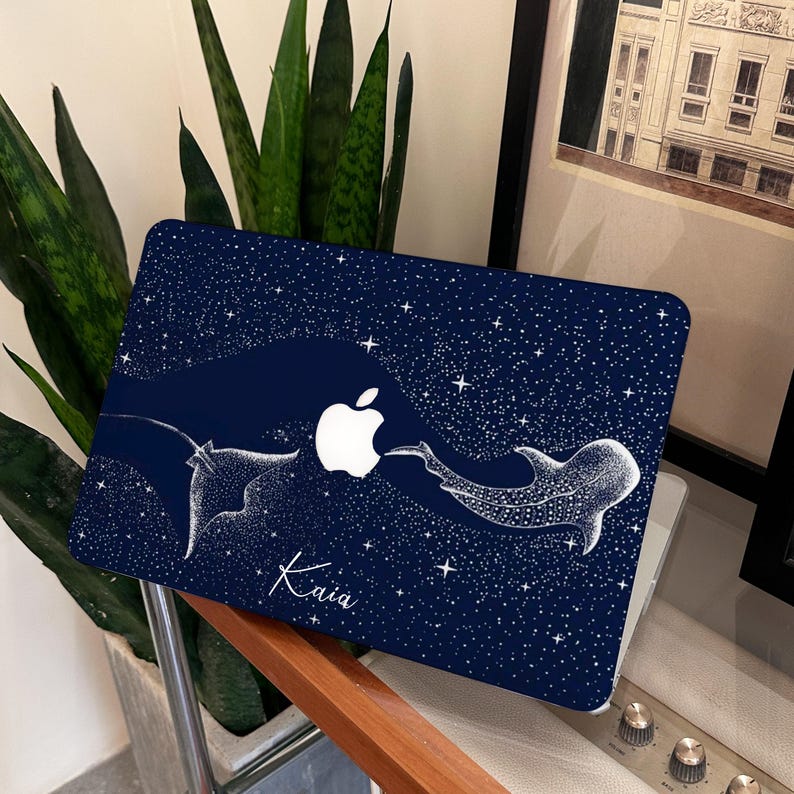 May include: A navy blue laptop case with a white Apple logo and a starry sky pattern. The case features a white illustration of a manta ray and a whale shark. The name "Kaia" is written in cursive.