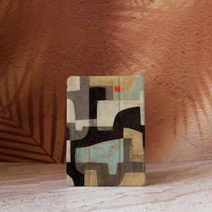 Puede incluir: Funda para tableta con diseño abstracto. La funda presenta un patrón geométrico en tonos negro, gris, beige y azul, con un pequeño acento rojo. La funda es rectangular con esquinas redondeadas.