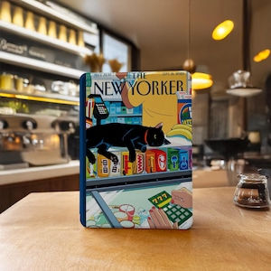 May include: A rectangular e-reader case featuring a New Yorker magazine cover illustration from 18 September 2023. The artwork depicts a black cat sleeping on a convenience store counter, with a hand scratching a 777 lottery ticket in the foreground.