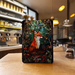 May include: A rectangular tablet case featuring a stained glass style illustration of a fox surrounded by green foliage and red flowers. The name Kaia is written in white cursive script at the bottom center of the colorful, intricate design.