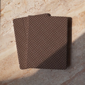 May include: A deck of cards with a brown background and a white polka dot pattern. The cards are fanned out slightly, revealing the design on the back. The cards are on a light brown surface.