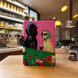 Peut inclure: Boîte métallique rectangulaire rose avec une illustration de deux chiens portant des lunettes de soleil et des foulards, dégustant du vin et des collations. Les chiens sont représentés sur une surface verte avec une bouteille de vin, des verres et de la nourriture. La boîte porte le mot "Kaja".